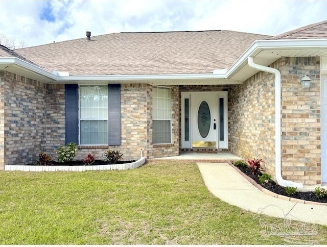 doorway to property with a yard, brick siding, and roof with shingles