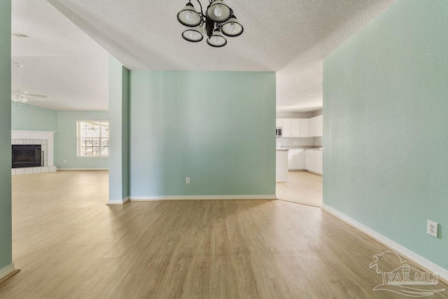 unfurnished living room with ceiling fan with notable chandelier, a textured ceiling, light wood-type flooring, and baseboards