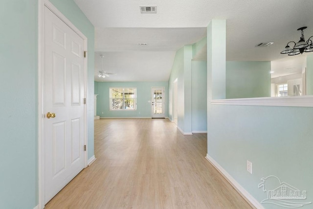 hallway with an inviting chandelier, light wood-style flooring, visible vents, and baseboards