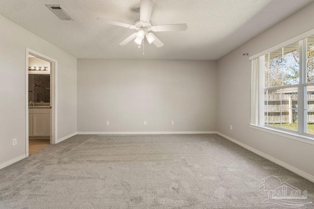 carpeted empty room with a textured ceiling, baseboards, visible vents, and ceiling fan