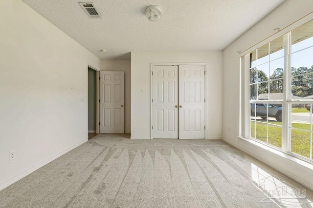 unfurnished bedroom featuring light carpet, multiple windows, a textured ceiling, and baseboards