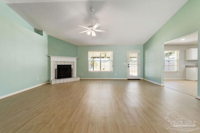 unfurnished living room with baseboards, light wood-style floors, a tile fireplace, and ceiling fan