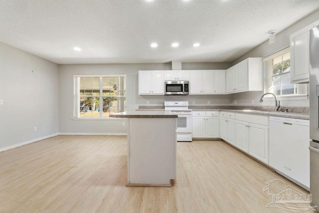 kitchen with white cabinetry, white appliances, light wood finished floors, and a textured ceiling