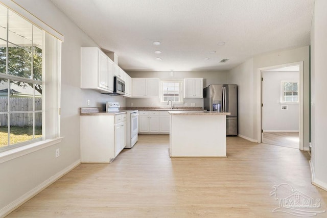 kitchen featuring a kitchen island, light wood-style flooring, a sink, stainless steel appliances, and white cabinets