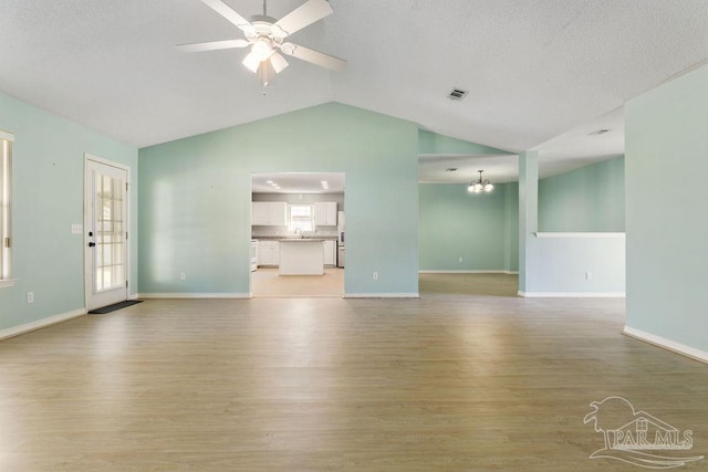 unfurnished living room with visible vents, baseboards, light wood-type flooring, vaulted ceiling, and ceiling fan with notable chandelier