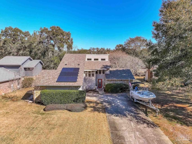 view of front of property with concrete driveway, a front yard, and roof mounted solar panels