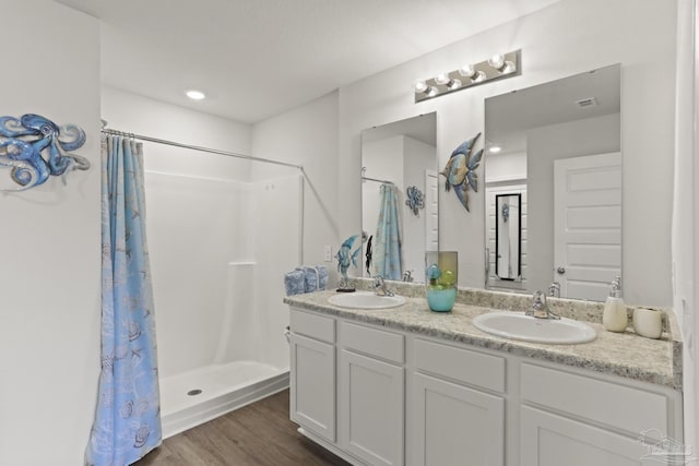 full bath with a shower with shower curtain, double vanity, a sink, and wood finished floors