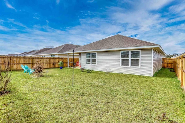 back of property with a shingled roof, a fenced backyard, and a lawn