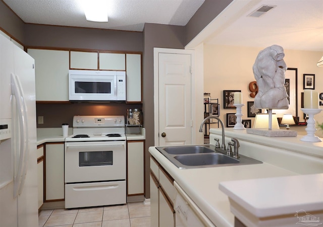 kitchen featuring sink, a textured ceiling, light tile patterned floors, white appliances, and white cabinets