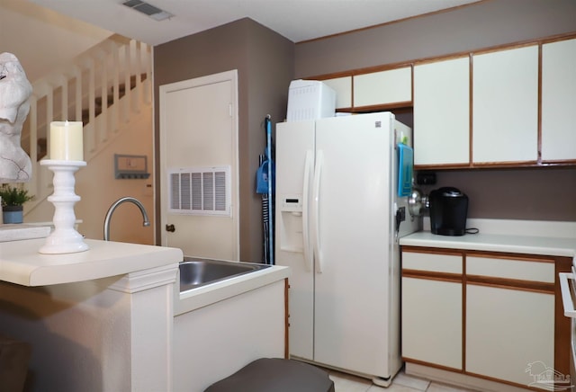 kitchen featuring white cabinets, light tile patterned floors, sink, and white fridge with ice dispenser