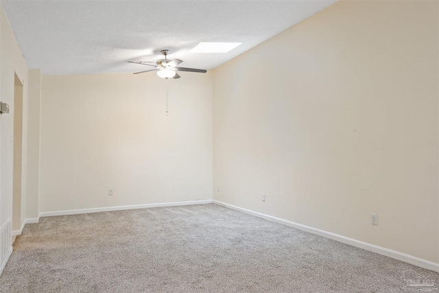 spare room with light colored carpet, ceiling fan, a skylight, and a textured ceiling