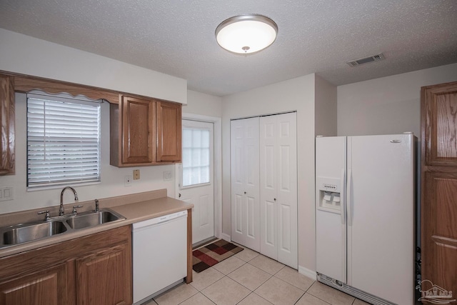 kitchen with a textured ceiling, white appliances, sink, and light tile patterned floors