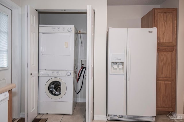 clothes washing area featuring light tile patterned flooring, stacked washer and dryer, and plenty of natural light