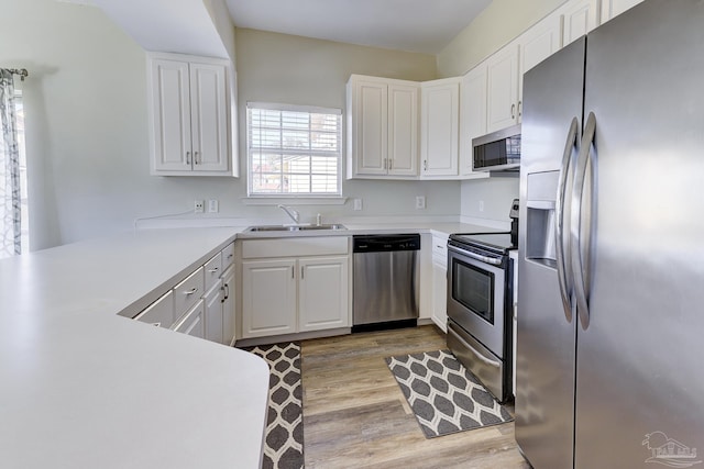 kitchen featuring appliances with stainless steel finishes, a sink, light wood-style floors, and white cabinets