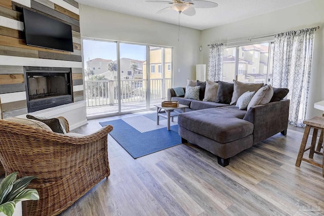 living area with a large fireplace, a textured ceiling, wood finished floors, and a ceiling fan