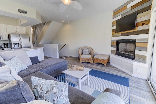 living area featuring a fireplace with raised hearth, a ceiling fan, visible vents, baseboards, and light wood-type flooring