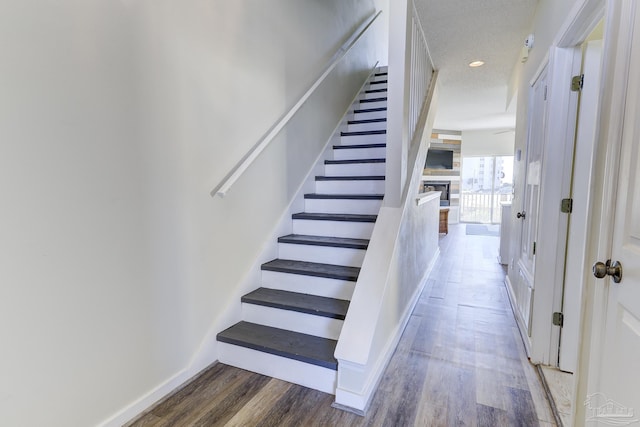 staircase featuring a stone fireplace, recessed lighting, wood finished floors, and baseboards