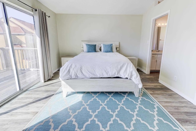 bedroom with baseboards, ensuite bathroom, wood finished floors, and access to exterior