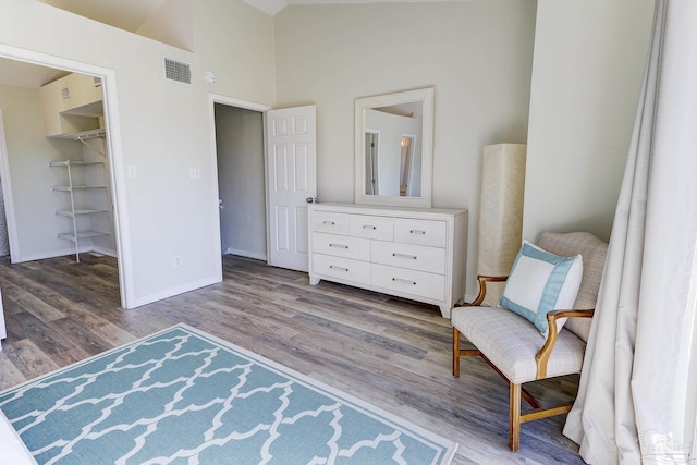 living area featuring a high ceiling, visible vents, baseboards, and wood finished floors