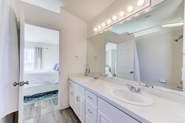 ensuite bathroom featuring a sink, double vanity, connected bathroom, and wood finished floors