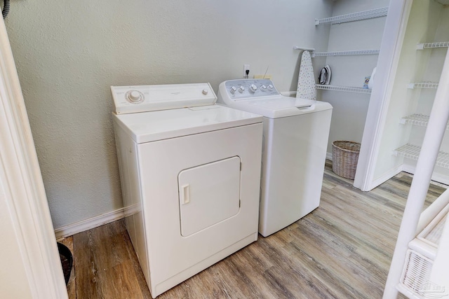 clothes washing area with laundry area, baseboards, a textured wall, light wood-style flooring, and washing machine and clothes dryer