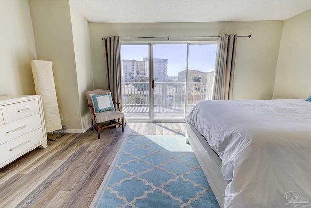 bedroom featuring baseboards, a textured ceiling, wood finished floors, and access to exterior