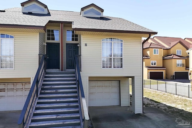 view of front facade with a shingled roof, fence, and an attached garage