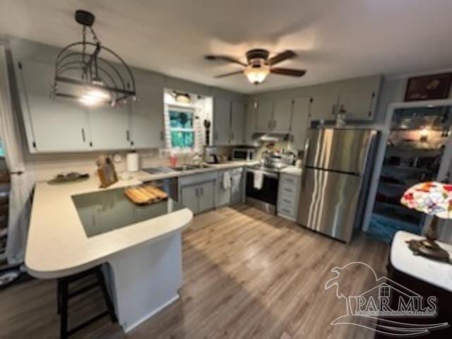 kitchen featuring hanging light fixtures, hardwood / wood-style flooring, ceiling fan, kitchen peninsula, and stainless steel appliances