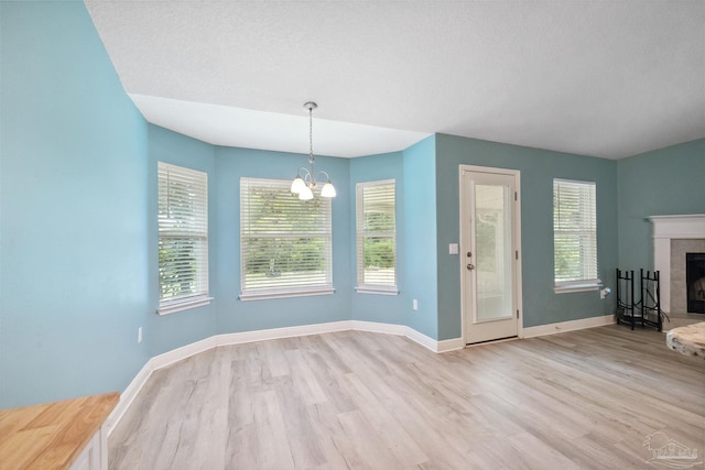 unfurnished dining area featuring an inviting chandelier, light hardwood / wood-style flooring, and a tile fireplace