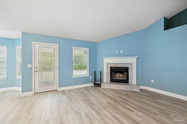 unfurnished living room with vaulted ceiling, light wood-type flooring, and a tile fireplace