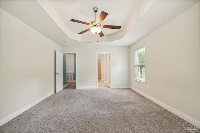 unfurnished bedroom with ceiling fan, light colored carpet, and a tray ceiling