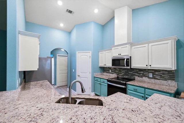 kitchen featuring appliances with stainless steel finishes, tasteful backsplash, sink, white cabinets, and a towering ceiling