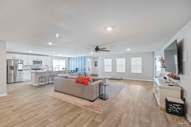 living room with a wealth of natural light, ceiling fan, a textured ceiling, and light hardwood / wood-style floors