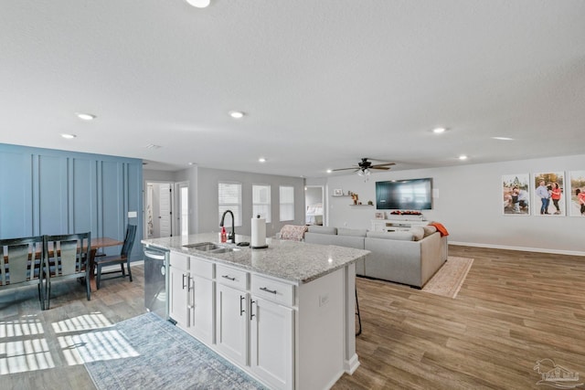 kitchen with light hardwood / wood-style floors, dishwasher, sink, an island with sink, and white cabinetry