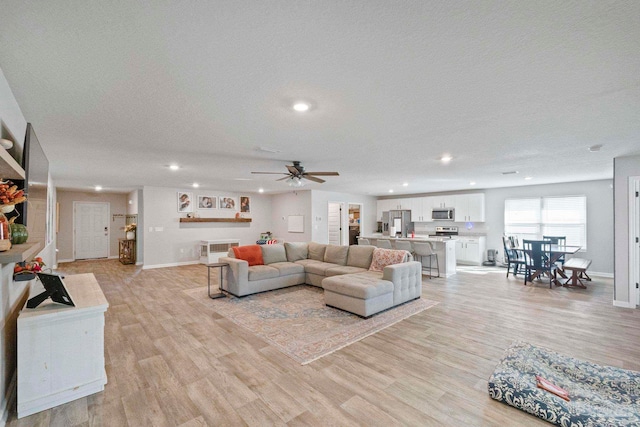 living room with ceiling fan, a textured ceiling, and light hardwood / wood-style floors