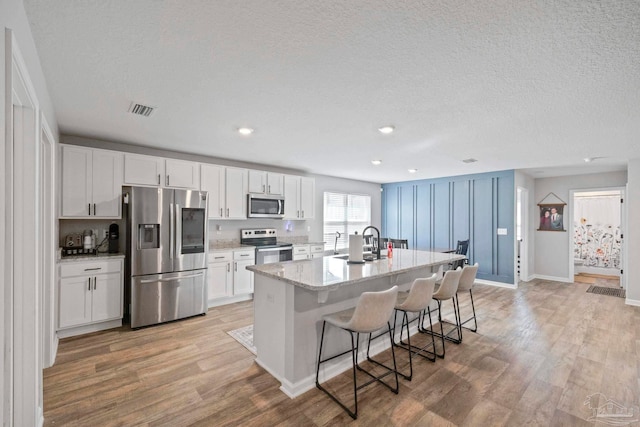 kitchen featuring light hardwood / wood-style floors, white cabinets, a breakfast bar area, a kitchen island with sink, and appliances with stainless steel finishes