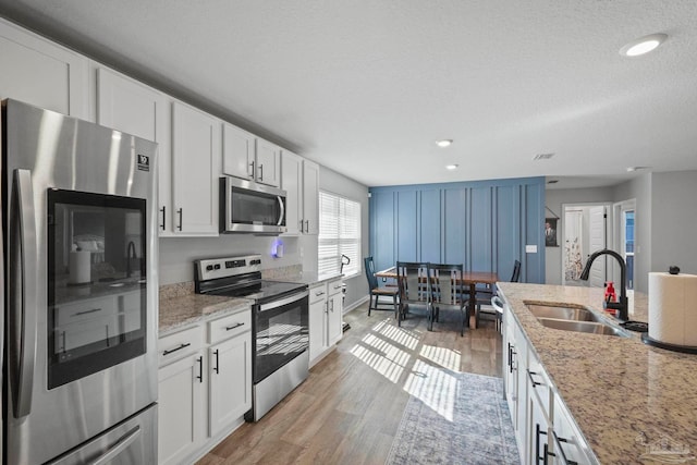 kitchen featuring stainless steel appliances, white cabinetry, sink, light stone countertops, and light hardwood / wood-style flooring