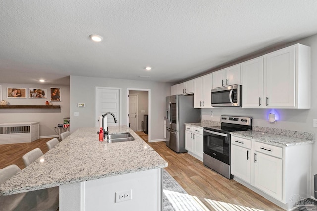 kitchen with a center island with sink, sink, a breakfast bar, light wood-type flooring, and appliances with stainless steel finishes