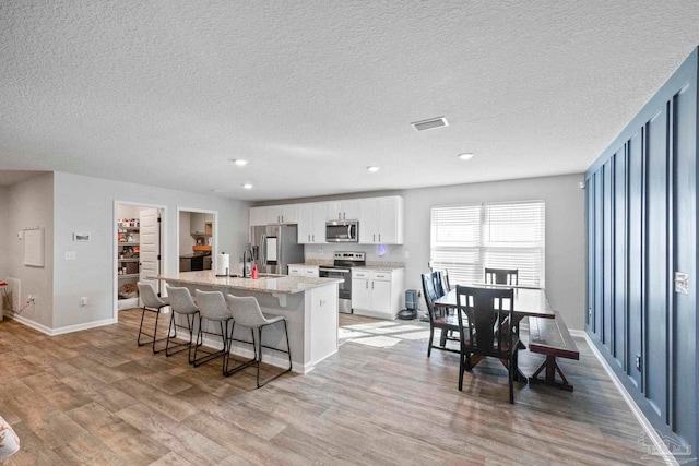 kitchen featuring a kitchen island, light wood-type flooring, appliances with stainless steel finishes, a kitchen bar, and white cabinets