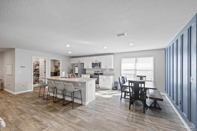 3897 James Stovall St, Pensacola, FL 32526 - kitchen with stainless steel appliances, a center island with sink, light wood-style flooring, a sink, and white cabinets