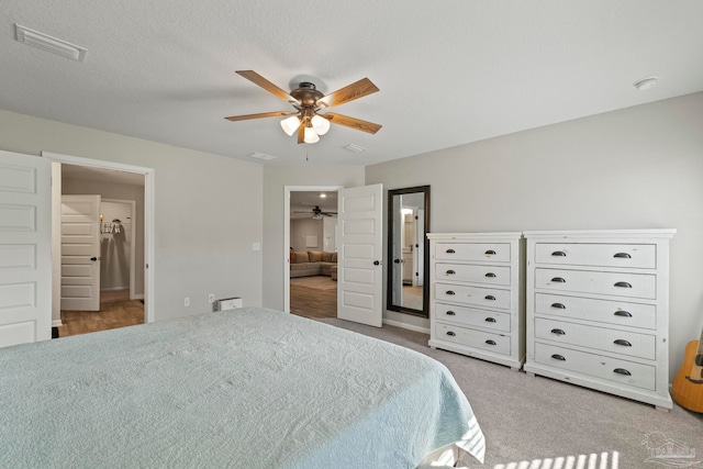 carpeted bedroom with ensuite bathroom, ceiling fan, a textured ceiling, a walk in closet, and a closet