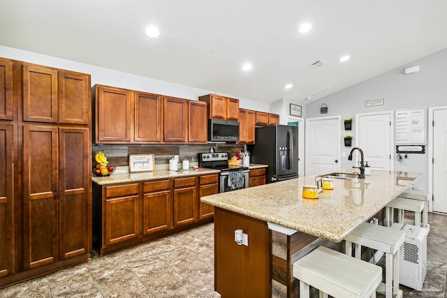 kitchen featuring vaulted ceiling, sink, stainless steel appliances, and a kitchen island with sink