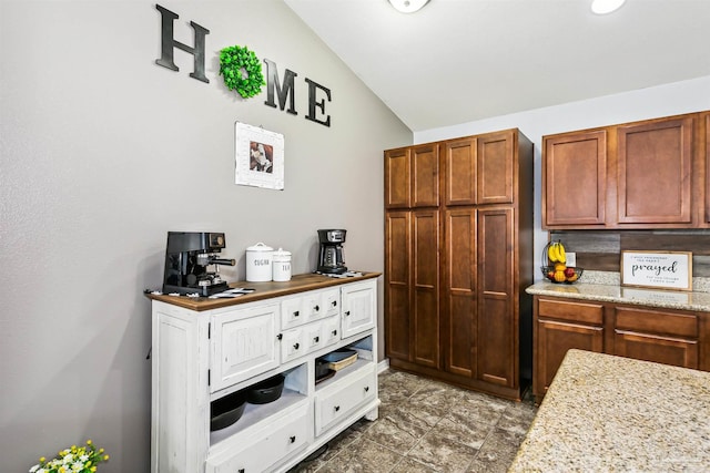 kitchen featuring tile patterned flooring, lofted ceiling, and light stone countertops