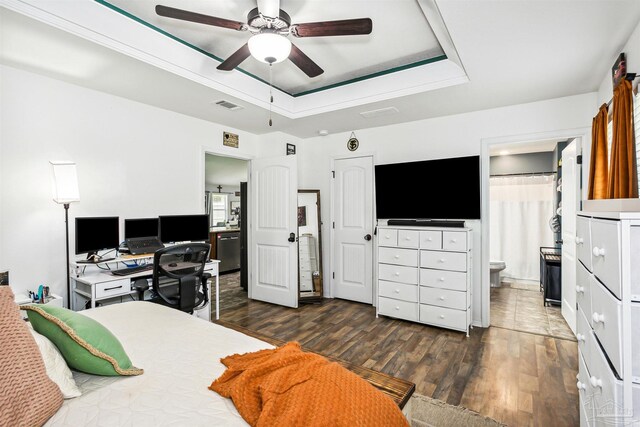 bedroom with ensuite bath, ceiling fan, dark hardwood / wood-style floors, and a tray ceiling