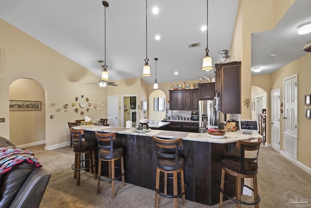 kitchen featuring a breakfast bar, pendant lighting, high vaulted ceiling, stainless steel fridge, and dark brown cabinets