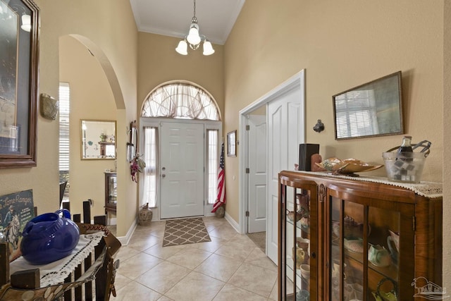 tiled foyer featuring crown molding, a towering ceiling, and an inviting chandelier