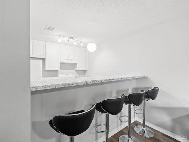 kitchen with under cabinet range hood, a textured ceiling, dark wood finished floors, and white cabinets