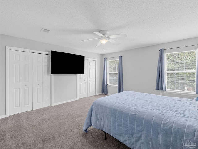 bedroom with visible vents, two closets, baseboards, ceiling fan, and carpet