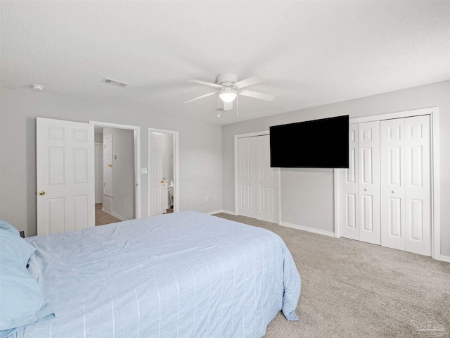 carpeted bedroom featuring visible vents, baseboards, multiple closets, a textured ceiling, and a ceiling fan