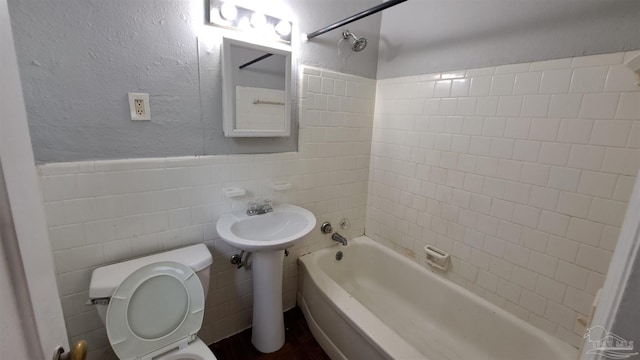 bathroom with tiled shower / bath combo, toilet, and tile walls